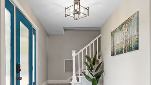Un couloir avec une porte bleue, un escalier, un tableau accroché au mur et un banc.