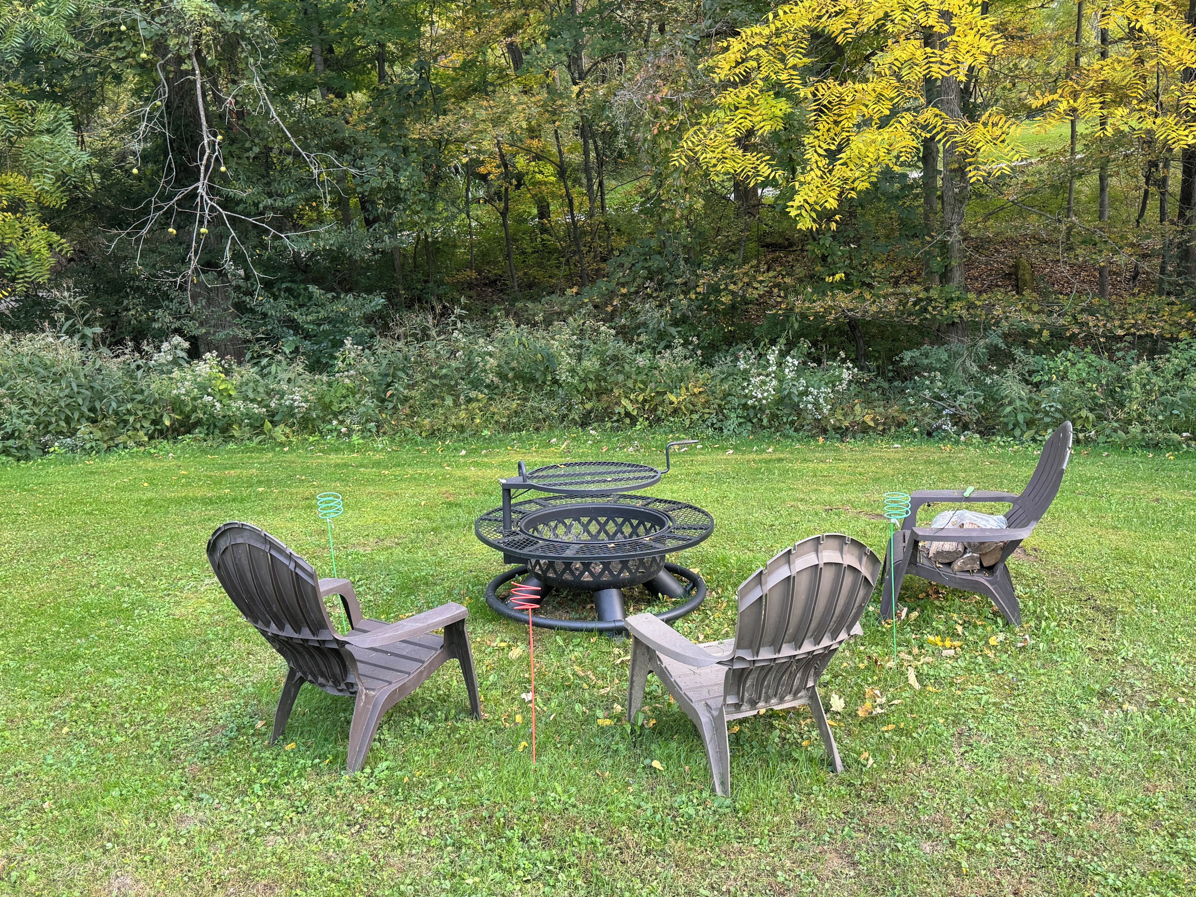Uma área de estar ao ar livre com uma mesa redonda e quatro cadeiras, cercada por um gramado e árvores.