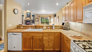 A kitchen with wooden cabinets, a dishwasher, a stove, and a window with a view of greenery.
