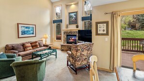 A cozy living room with a fireplace, comfortable seating, and large windows offering a view of the outdoors.