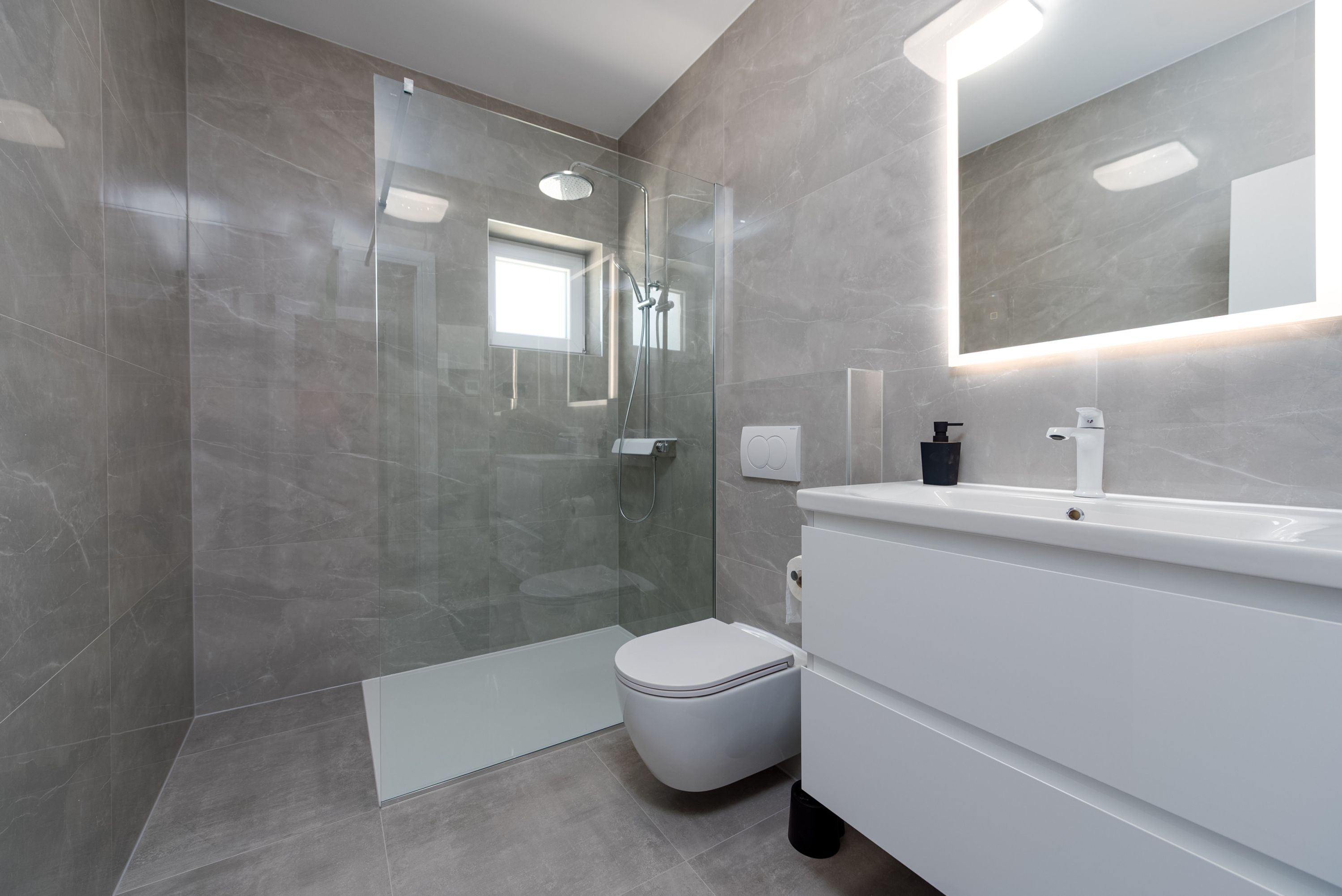 A modern bathroom with a glass-enclosed shower, a white toilet, and a vanity with a mirror.