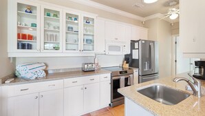 A modern kitchen with white cabinetry, a stainless steel refrigerator, a microwave, and a gas stove. - Updated Cottage Steps to the Beach, Pool and Beach Gear (Holmes Beach)