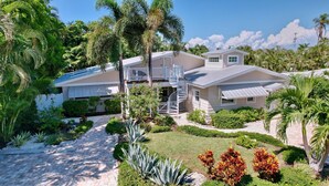 A two-story house with a covered patio, a spiral staircase, and a well-maintained garden with palm trees and shrubs.