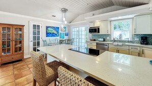 A spacious kitchen with a large island, modern appliances, and a dining area with wicker chairs.