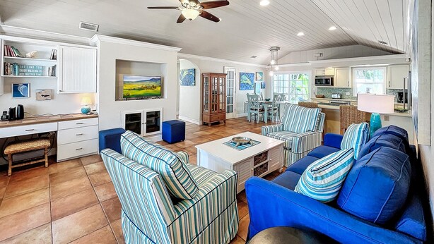 A spacious living area with a large blue sofa, striped armchairs, a dining table, and a ceiling fan.