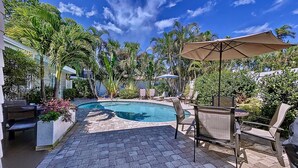 A swimming pool with lounge chairs and umbrellas, surrounded by lush greenery and a clear blue sky.