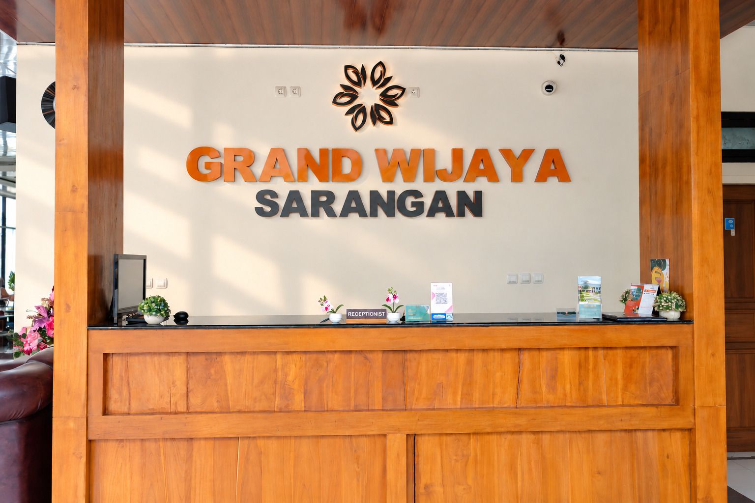 A reception desk with the sign 'Grand Wijaya Sarangan' and a logo above it.