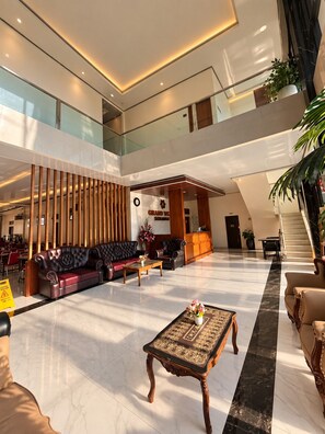 A spacious lobby with a high ceiling, a reception desk, seating area, and a staircase leading to an upper level.