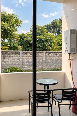 A balcony with a glass table and chairs, a brick wall, and an air conditioning unit. - Grand Wijaya Hotel dan Villa Sarangan (Plaosan)