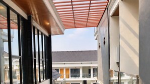 A modern building with a covered outdoor seating area, glass railings, and a view of a residential building in the background. - Grand Wijaya Hotel dan Villa Sarangan (Plaosan)