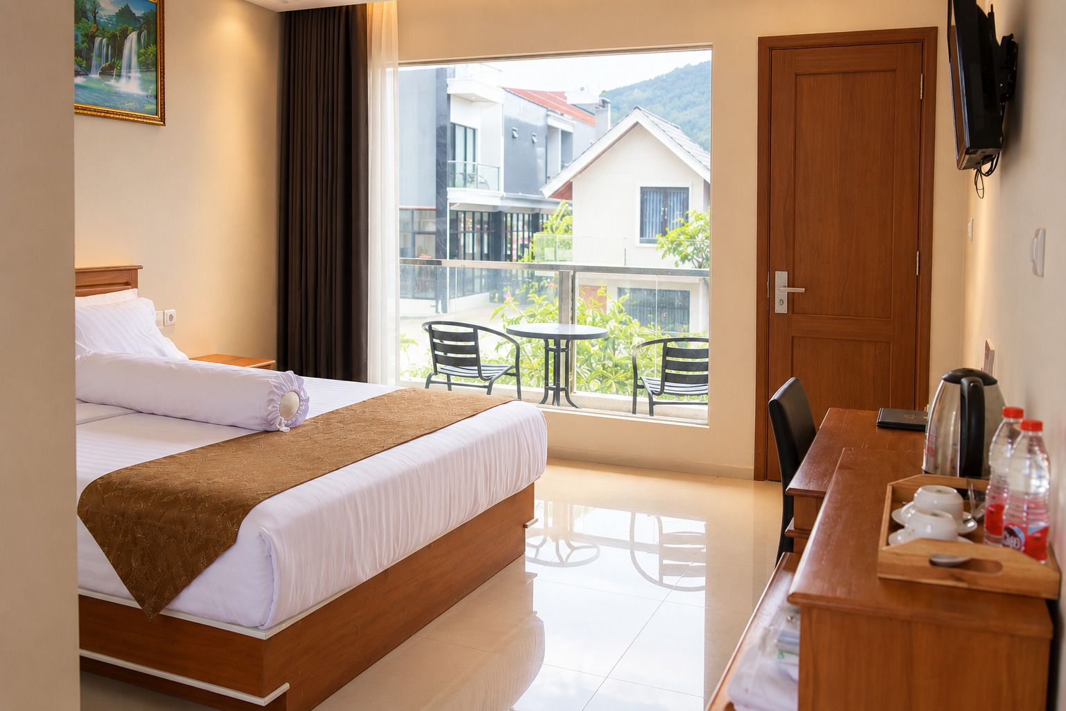 Ein Hotelzimmer mit einem Bett, einem Schreibtisch mit Kaffeemaschine, einem Fernseher und einem Balkon mit Stühlen und Tisch.