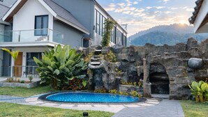 A modern house with a swimming pool, a stone wall, and a view of the mountains. - Grand Wijaya Hotel dan Villa Sarangan (Plaosan)