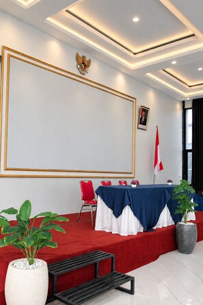 A conference room with a large whiteboard, red and white chairs, a table with a blue tablecloth, and a flag. - Grand Wijaya Hotel dan Villa Sarangan (Plaosan)