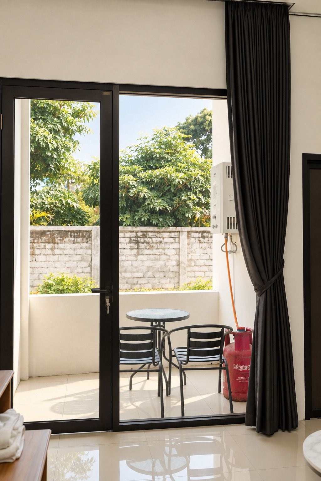 Une pièce dotée d’une porte-fenêtre coulissante donnant sur un espace extérieur aménagé avec une table et des chaises, un mur en briques et de la verdure.