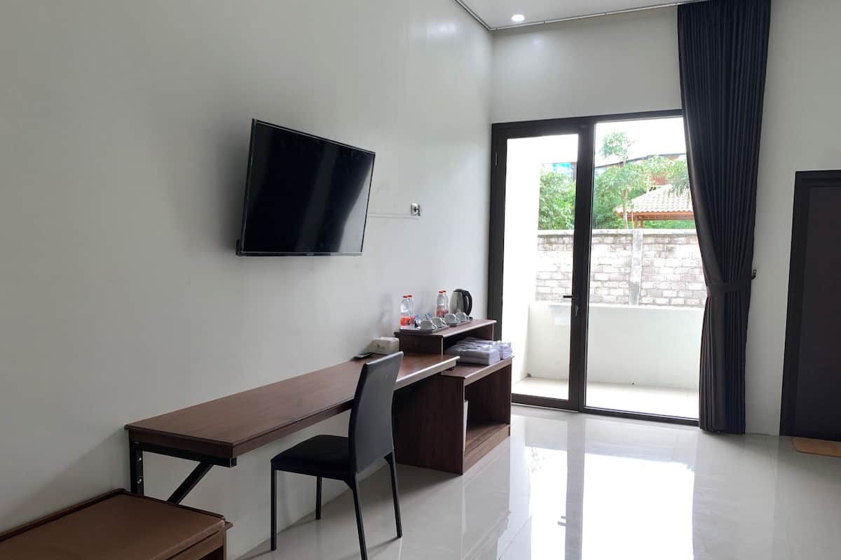 Quarto moderno com televisão de tela plana na parede, escrivaninha de madeira com cadeira, mesinha e porta de vidro deslizante para área externa.