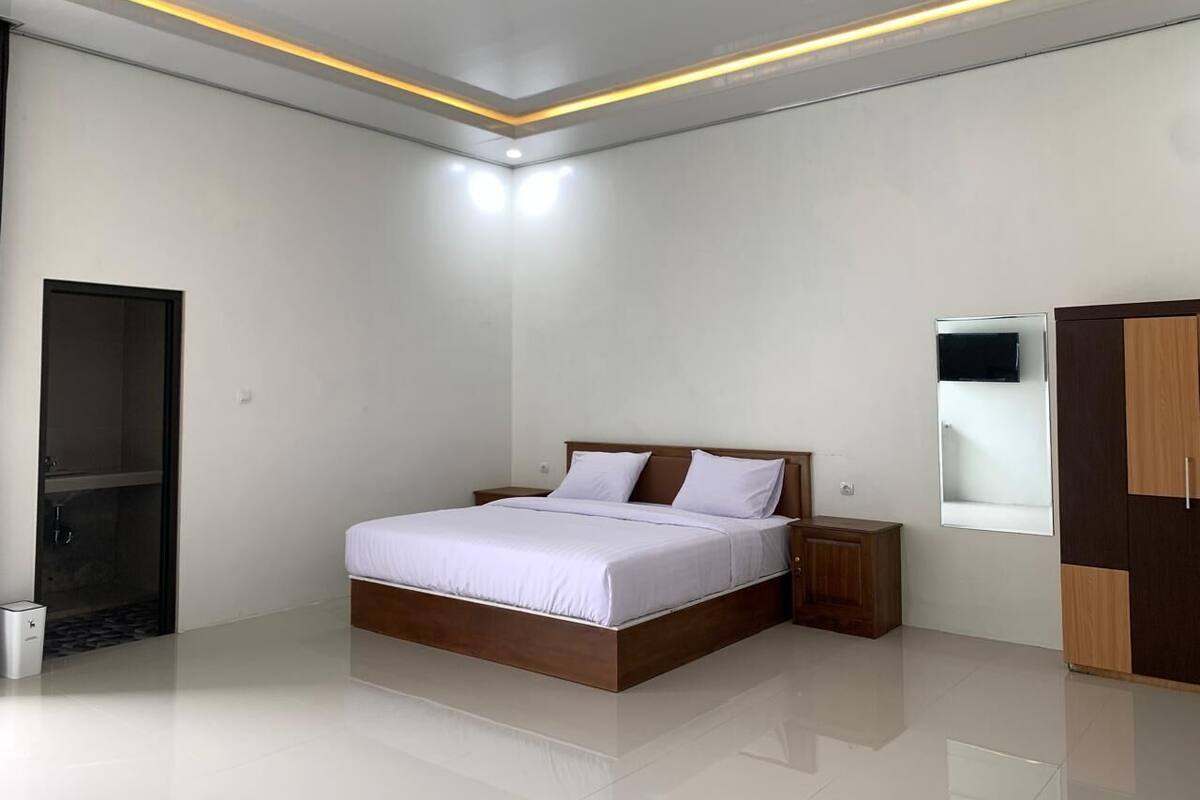 Quarto moderno com cama grande, mesas de cabeceira, guarda-roupa e televisão embutida.