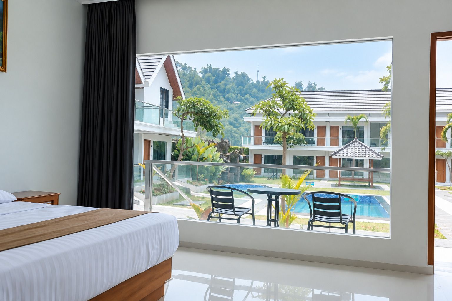 A hotel room with a bed, a glass table, and a view of a swimming pool and buildings.