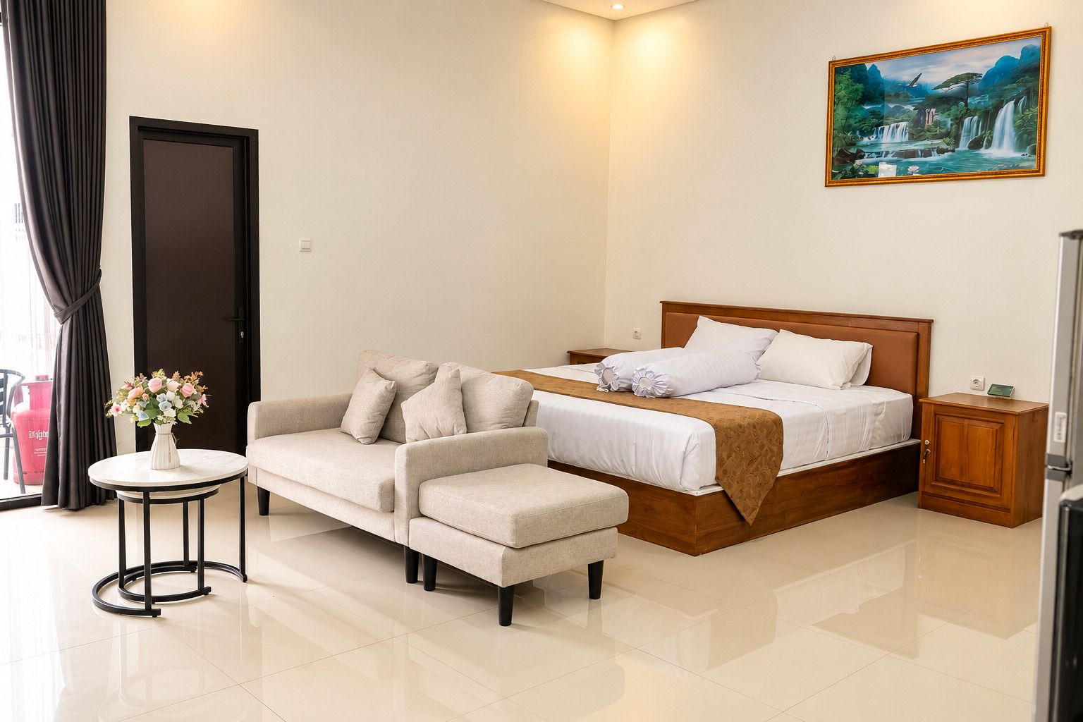A hotel room with a bed, a sofa, a small table with a vase of flowers, and a painting on the wall.