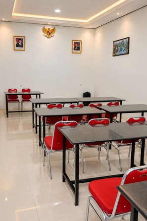A conference room with multiple tables and red chairs, featuring framed portraits and an emblem on the wall. - Grand Wijaya Hotel dan Villa Sarangan (Plaosan)