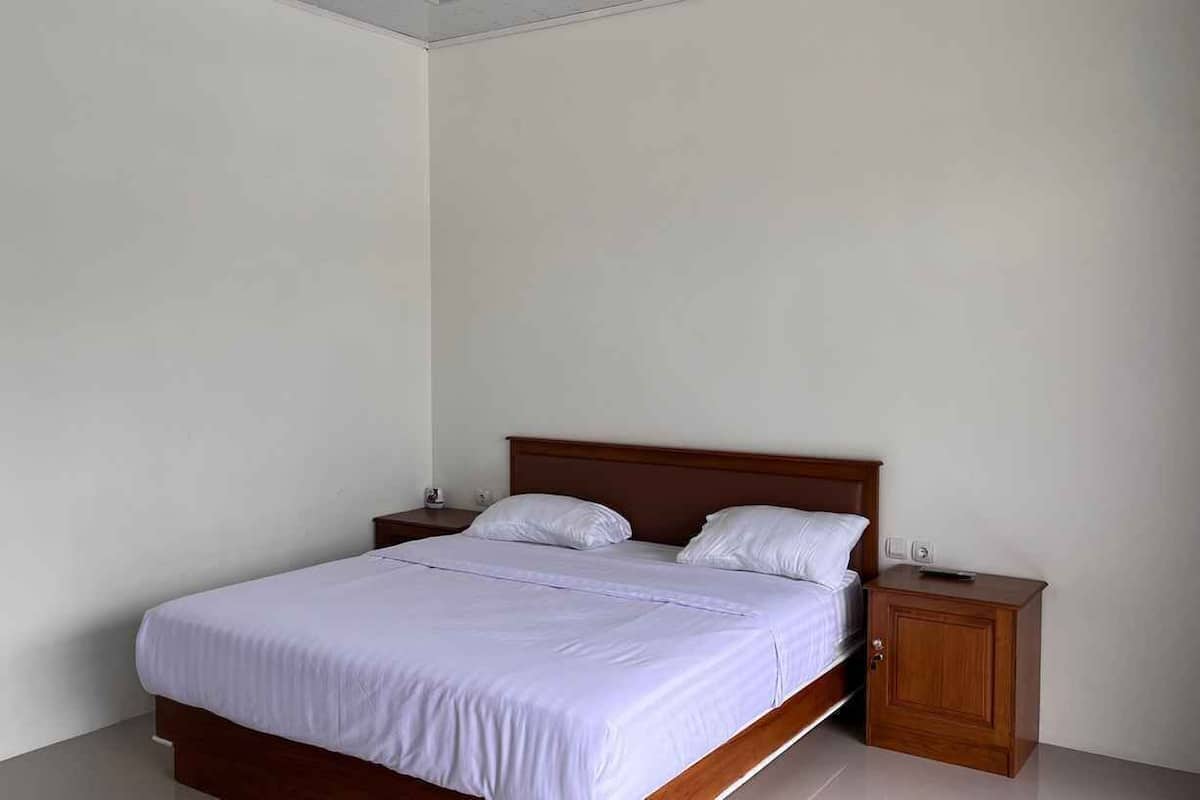 Uma cama de solteiro com cabeceira de madeira em um quarto com paredes brancas e uma pequena mesa de cabeceira ao lado.