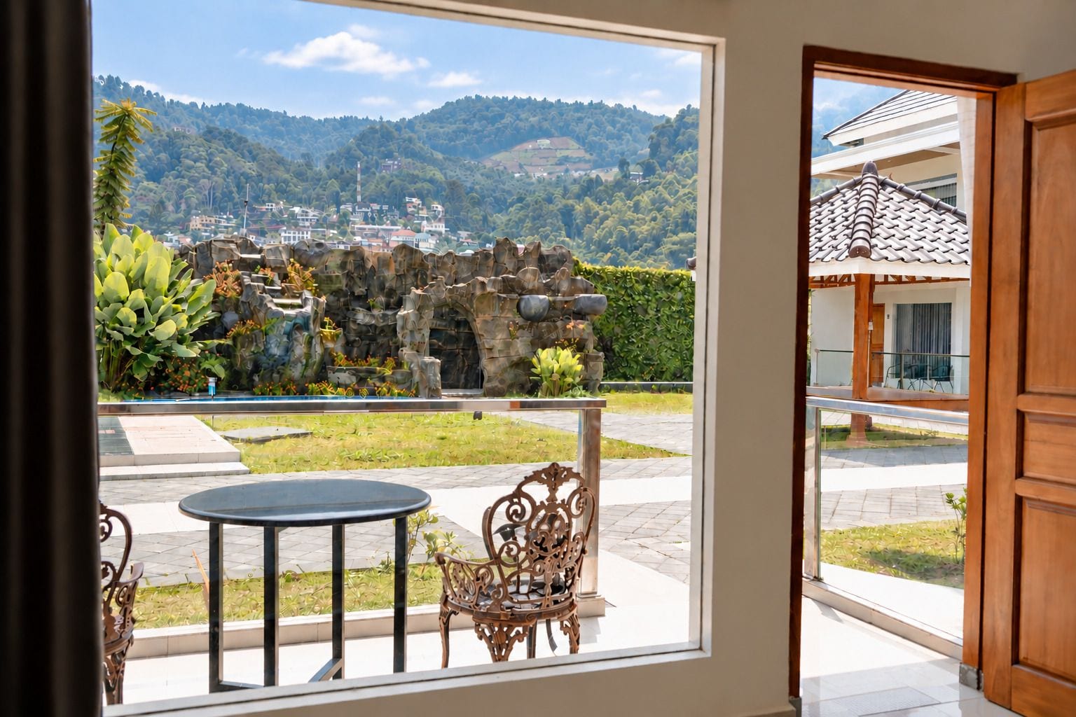 A room with a view of a mountainous landscape, a stone wall, and a small garden with a table and chairs.