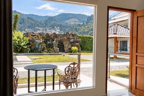 A room with a view of a mountainous landscape, a stone wall, and a small garden with a table and chairs. - Grand Wijaya Hotel dan Villa Sarangan (Plaosan)