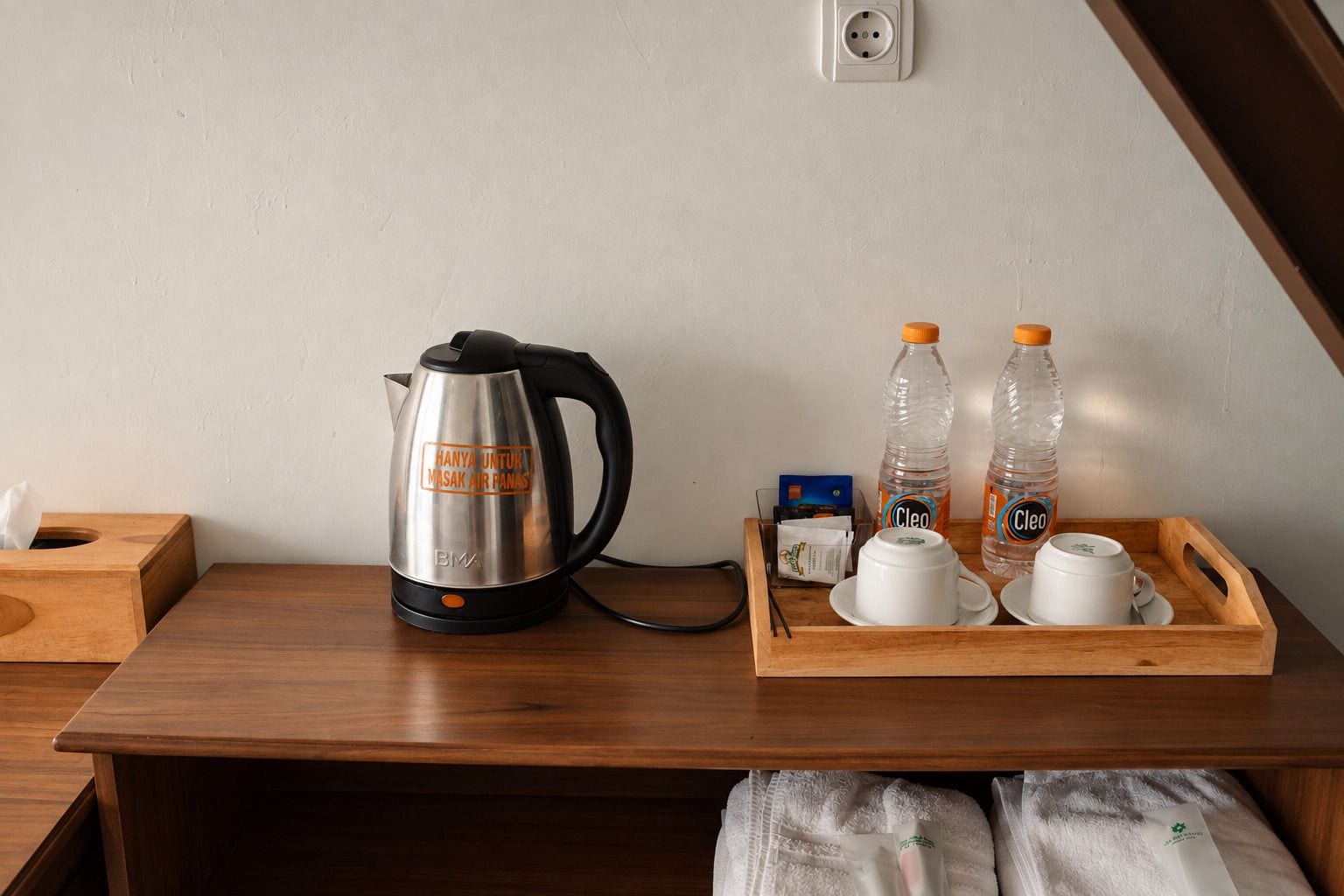 A wooden table with a kettle, two bottles of water, and a tray with cups and a tissue box.