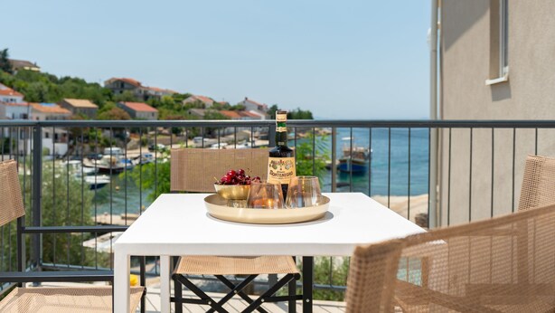 Ein Balkon mit Tisch für zwei Personen, Blick auf einen Yachthafen und eine Küstenstadt.