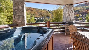 A hot tub on a wooden deck with stone pillars, overlooking a scenic hillside with autumn foliage.