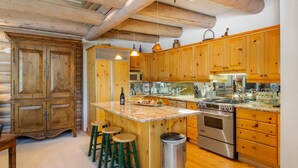 Una cucina rustica con mobili in legno, un'isola centrale con sgabelli, un piano cottura in acciaio inossidabile e un cestino.