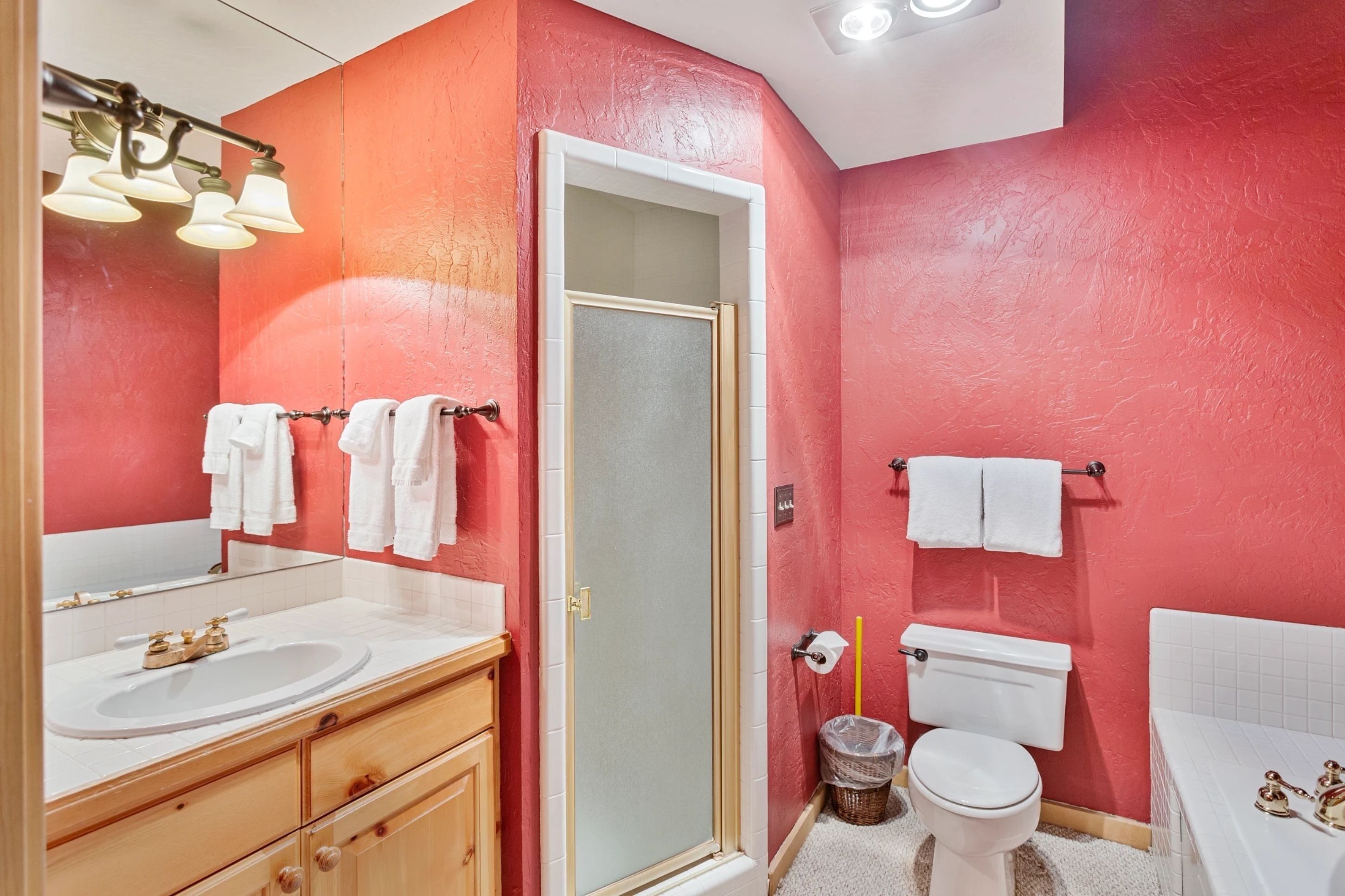 Un baño con pared roja, lavamanos blanco y bañera.