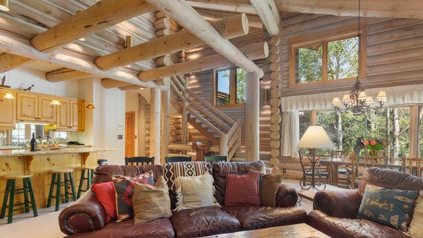 Interno di una baita di legno con un divano in pelle, un tavolo da pranzo in legno e un angolo cucina con sgabelli.