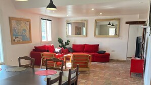 A dining area with a table and chairs, a red sofa, and a television on a stand. - Le Grand mazet (ARLES)