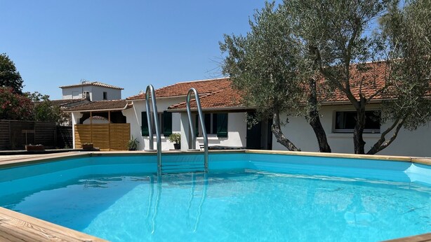 A rectangular swimming pool with a wooden deck edge, surrounded by a fence and trees. - Le Grand mazet (ARLES)