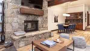 A stone fireplace with a flat-screen TV above it, a dining area with blue chairs, and a kitchen with wooden cabinets. - Trail's End Lodge at Deer Valley Resort - Two Bedroom Residence with Spa #402 2 Condo (Park City)