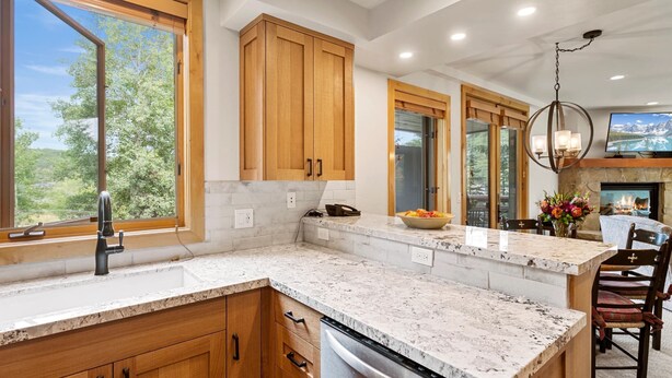 A modern kitchen with wooden cabinets, a granite countertop, a stainless steel dishwasher, and a large window offering a view of greenery. - Trail's End Lodge at Deer Valley Resort - One Bedroom Residence with Spa #205 1 Condo (Park City)