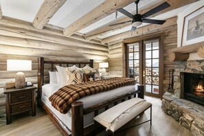 A log cabin bedroom with a bed, bench, bedside table, fireplace, and a view through a glass door. - Pine Inn at Trail's End Lodge - Two Bedroom Condo Residence with Spa #7 by Deer Valley Resort (Park City)