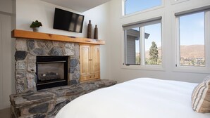 A bedroom with a stone fireplace, wooden cabinets, a TV mounted above the fireplace, and large windows offering a view of the outdoors. - Trail's End Lodge at Deer Valley Resort - Three Bedroom Residence with Spa #506 3 Condo (Park City)