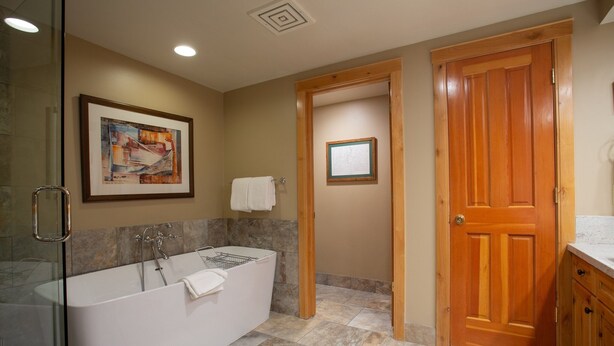 Un baño moderno con una bañera independiente, cabina de ducha con paredes de vidrio y una puerta de madera.