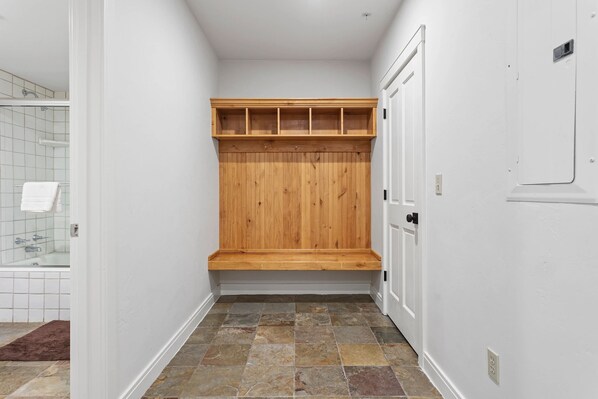 A narrow hallway with a wooden bench, a white door, and a tiled shower area.
