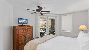Una camera da letto con un letto, una cassettiera in legno, una televisione, una ventola a soffitto, una finestra e una lampada.