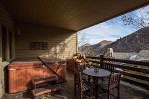 Eine Holzterrasse mit Whirlpool, Tisch und Stühlen, mit Blick auf eine Berglandschaft.
