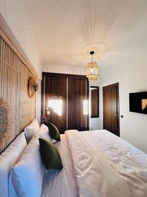 A bedroom with a large bed, a wooden headboard, a hanging light fixture, and a wardrobe. -  Authentic Apartment in Gueliz  Marrakesh (Marrakesh)