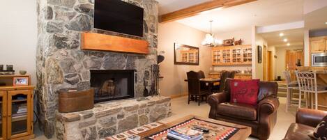 A cozy living room with a stone fireplace, wooden furniture, and a dining area.