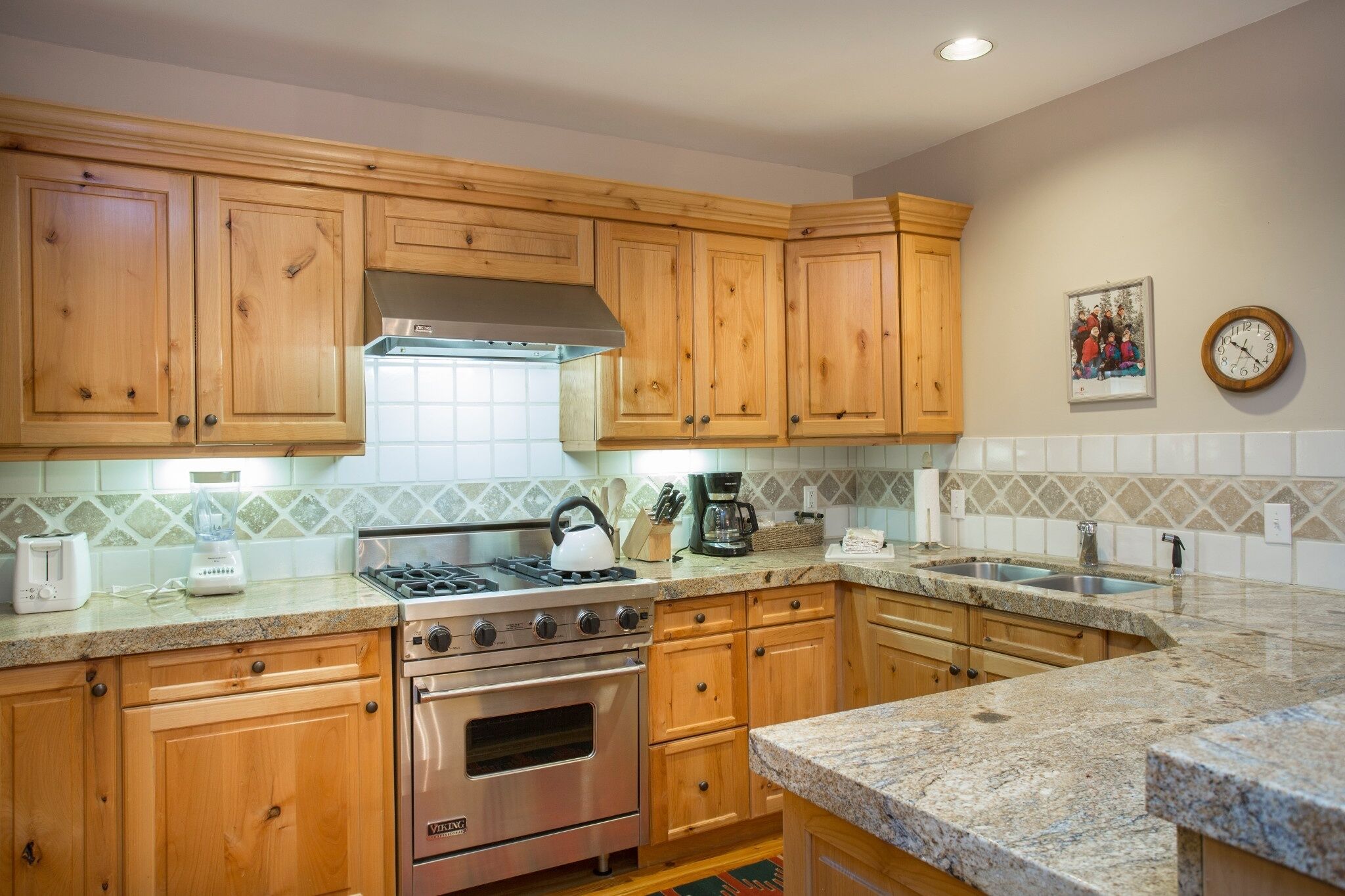 Una cocina con gabinetes de madera, estufa a gas, horno, cafetera y pileta.