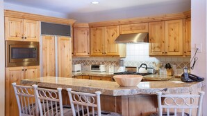 A kitchen with wooden cabinets, a granite countertop, a built-in microwave, a stove, and a sink. There are four white chairs around the island. - Trail's End Lodge at Deer Valley Resort - Two Bedroom Residence with Spa #406 2 Condo (Park City)