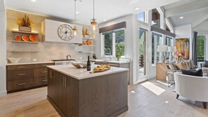 A modern kitchen with a large island, wooden cabinets, and a built-in clock.