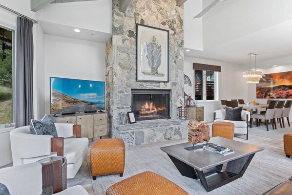 A modern living room with a stone fireplace, comfortable seating, a flat-screen TV, and a dining area with a chandelier. - Trail's End Lodge at Deer Valley Resort - Four Bedroom Residence with Spa #15 4 Condo (Park City)