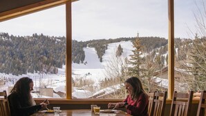 A dining area with a large window overlooking a snowy landscape with trees and a lake. - Trail's End Lodge at Deer Valley Resort - One Bedroom Deluxe Residence with Spa #304 1 Condo (Park City)