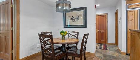 A dining area with a round wooden table, four chairs, a vase with flowers, and a framed picture on the wall.